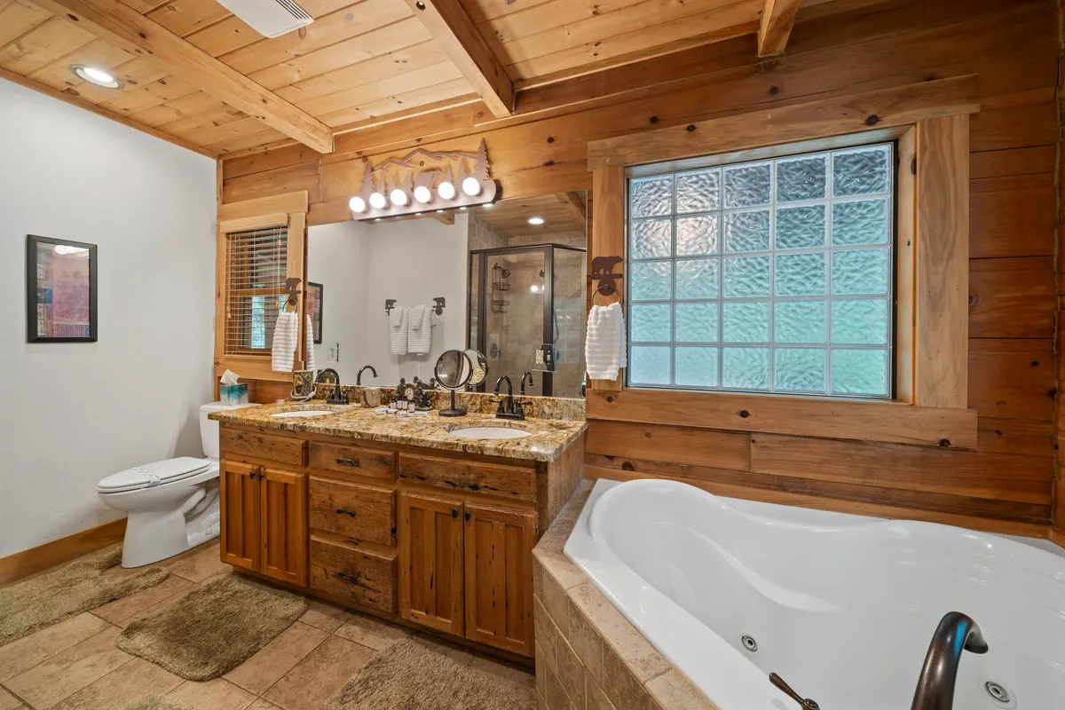 A spa-inspired bathroom featuring a freestanding bathtub, double granite vanity, and a large frosted window that offers privacy while letting in soft, natural light. The space exudes warmth and luxury, ideal for unwinding after an adventurous day.