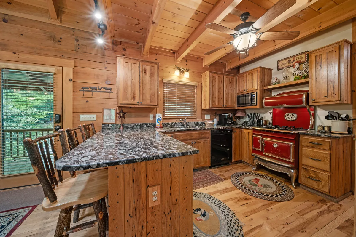 A view of the kitchen showcasing the red vintage stove, granite countertops, wooden bar stools lined up at the counter, and an open window letting in natural light. The space feels inviting and functional, ideal for both cooking and casual gatherings.