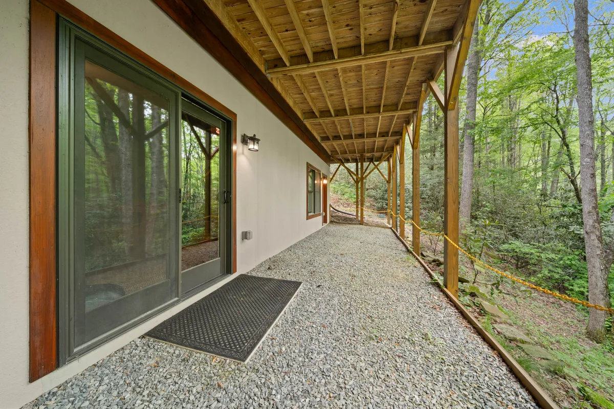 A welcoming view of the cabin’s front entrance, with a gravel pathway leading to a rustic wooden porch framed by sturdy beams and surrounded by trees. The setting exudes privacy, natural beauty, and upscale mountain living from the moment of arrival.