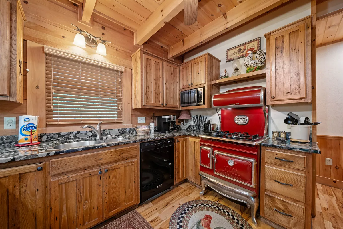 A warmly lit kitchen scene featuring the striking red Elmira antique-style stove, granite countertops, wooden cabinets, and a collection of decorative shelf items. The setting radiates nostalgia and culinary inspiration, inviting guests to cook and gather.