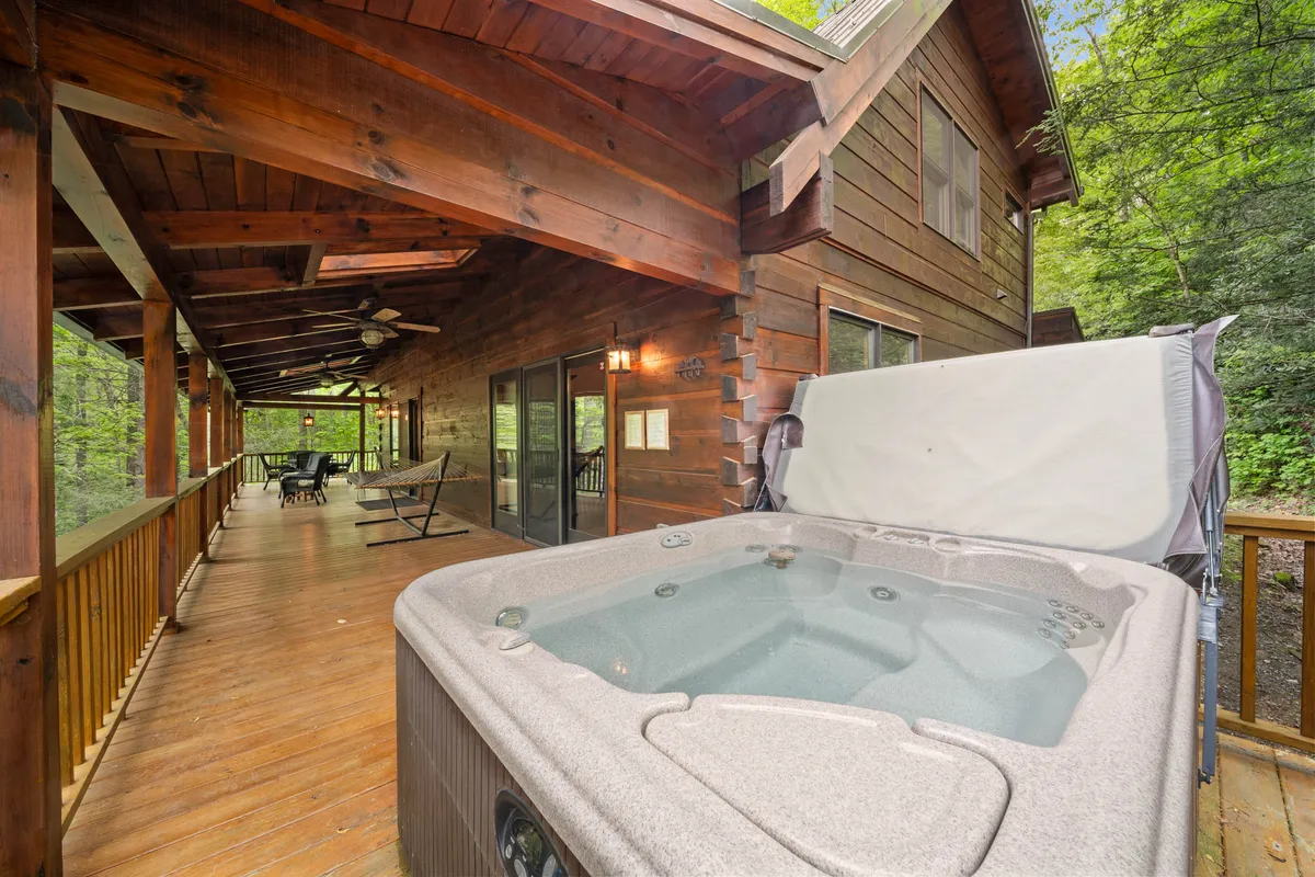 A tranquil exterior scene featuring a bubbling hot tub on a wooden deck, set against a backdrop of greenery. The inviting space is perfect for both daytime relaxation and evening stargazing, representing one of the cabin’s signature amenities.